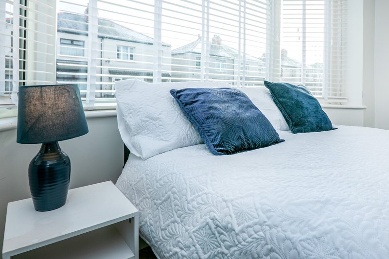 Bright bedroom with white bed, blue and teal pillows, bedside lamp and city views