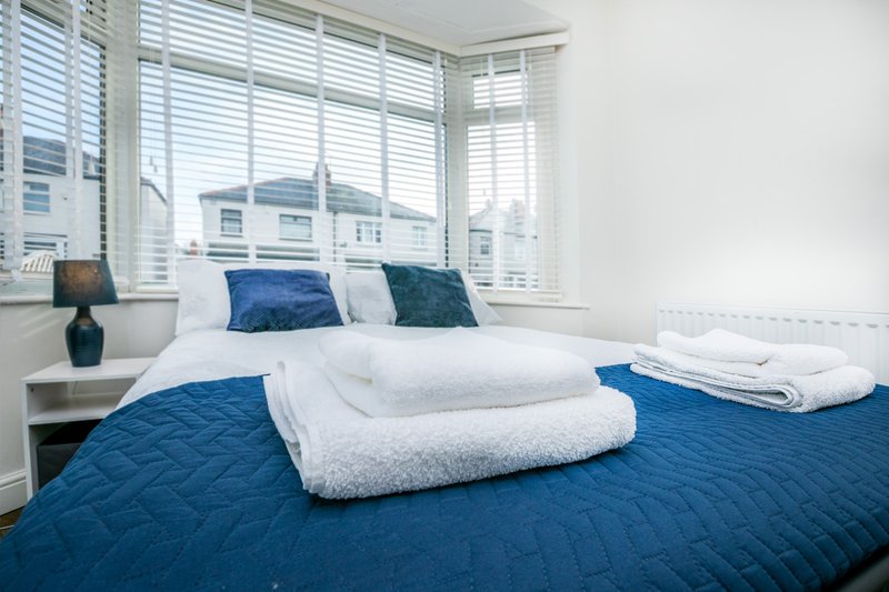 Bright bedroom with double bed, blue bedding, white pillows and folded towels, large windows with shutters