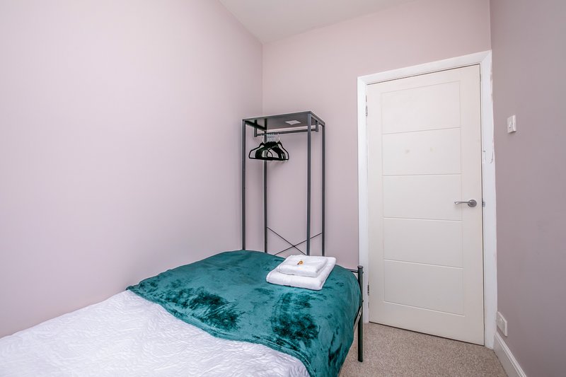 Bedroom with white and teal bedding, metal frame bed, pendant lamp, and white door.