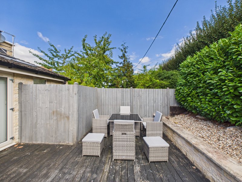 Outdoor patio with rattan furniture set, wooden decking, and hedged garden borders