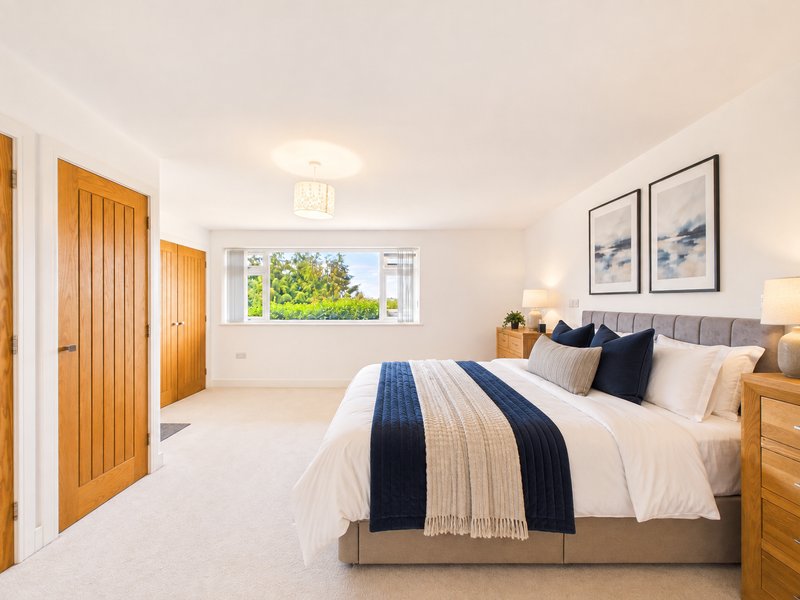 Spacious bedroom with double bed, wooden wardrobes, framed wall art and window view