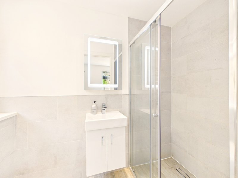 Modern bathroom with white vanity, illuminated mirror, glass shower enclosure and neutral tile