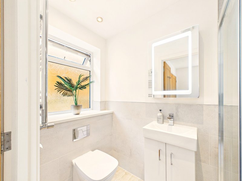 Modern bathroom with wall-mounted sink, illuminated mirror, toilet, and window with plant