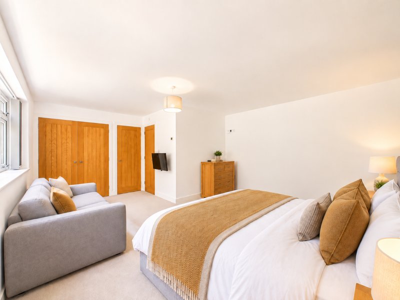 Spacious bedroom with double bed, seating area, wooden wardrobe and natural lighting