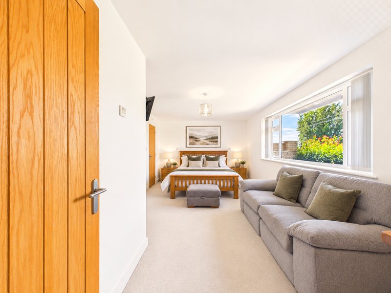 Spacious bedroom with wooden bed, grey sofa, large windows overlooking garden