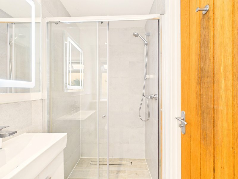 Modern bathroom with walk-in shower, white vanity sink and wooden door