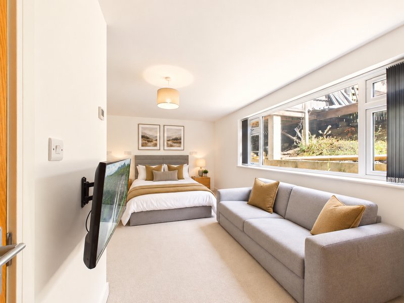 Modern bedroom with double bed, sofa seating, large windows and wooden door frame