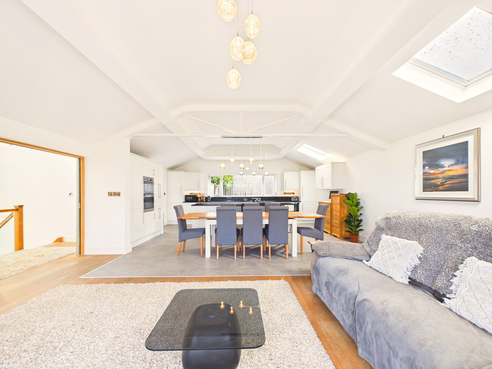 Open-plan living area with dining table, kitchen, sofa, pendant lights and skylights