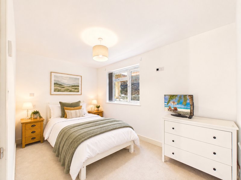 Bright bedroom with double bed, wooden dresser, white chest of drawers, and framed landscape artwork