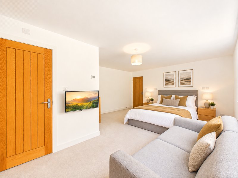 Spacious bedroom with double bed, sofa, wooden door and framed wall art