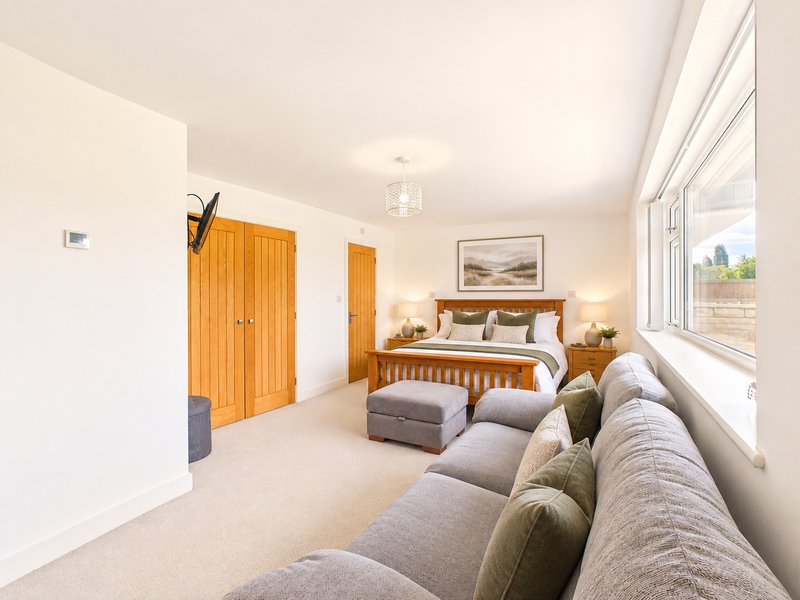 Bright bedroom with wooden bed, grey upholstered sofa, large windows and wooden wardrobe