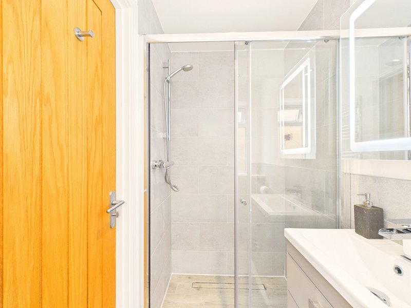 Modern bathroom with walk-in shower, white vanity, mirror and wooden door
