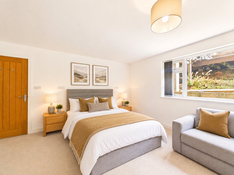 Bright bedroom with double bed, wooden nightstands, armchair and framed wall art