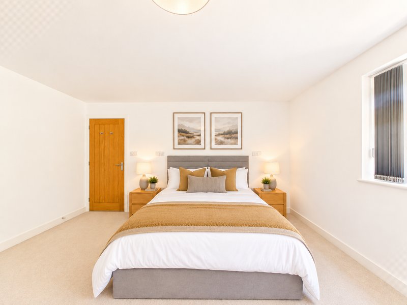Bright modern bedroom with double bed, wooden bedside tables, wall art and carpeted flooring