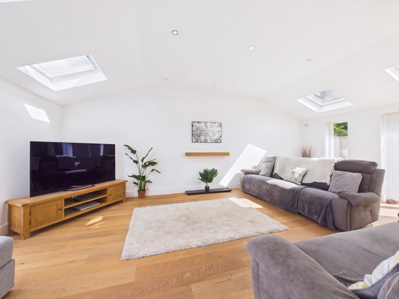 Bright open-plan living room with wooden flooring, skylight, TV unit, grey sofa and armchair