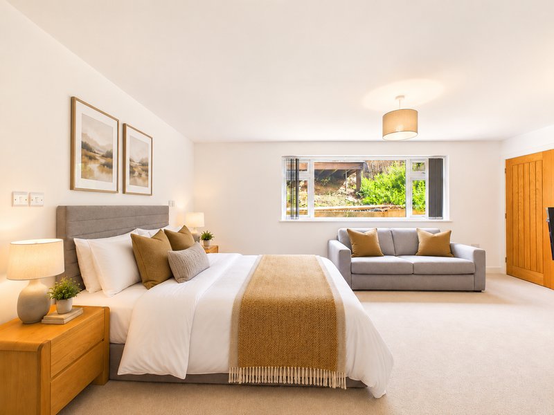 Spacious bedroom with double bed, wooden nightstands, sitting area with sofa and large window overlooking garden
