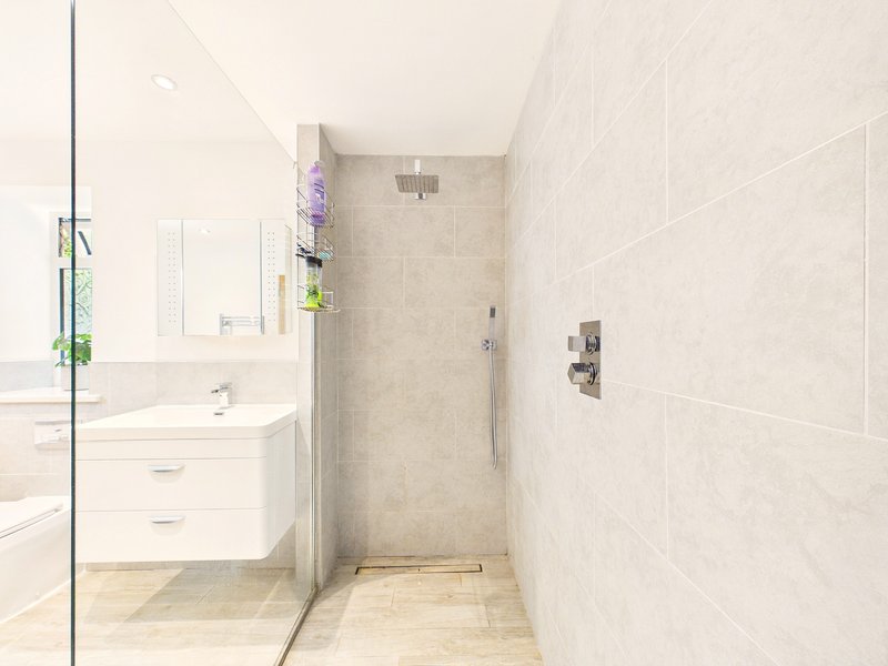 Modern bathroom with walk-in shower, white vanity sink, and light tile walls