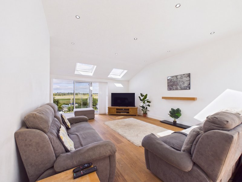 Bright modern living room with grey armchairs, wooden floor, TV, and countryside views through large windows