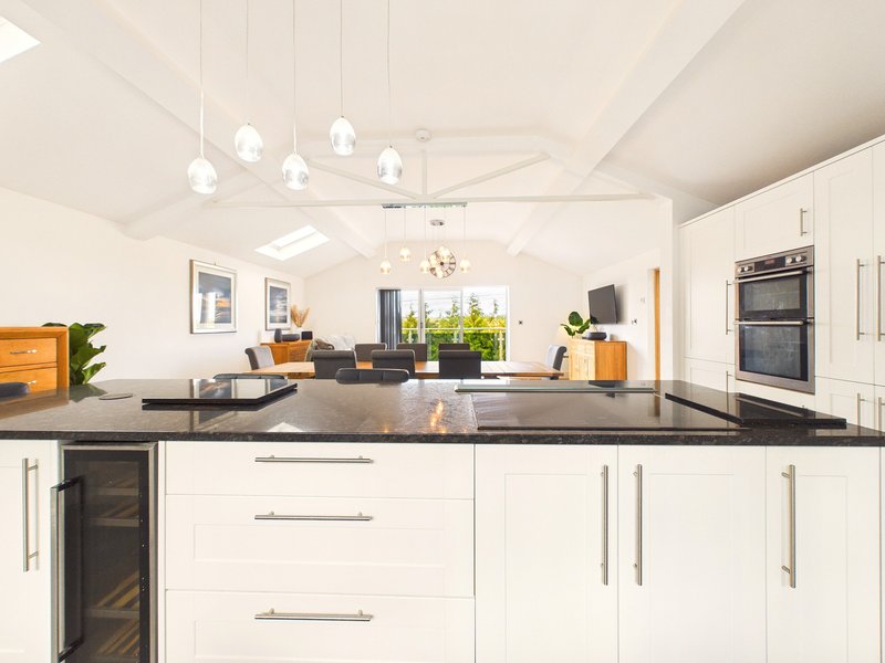 Modern open-plan kitchen with white cabinetry, dark countertops, island seating, and pendant lighting