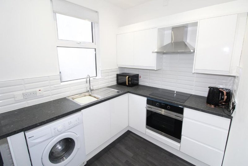 Modern white kitchen with black countertops, integrated appliances and washing machine