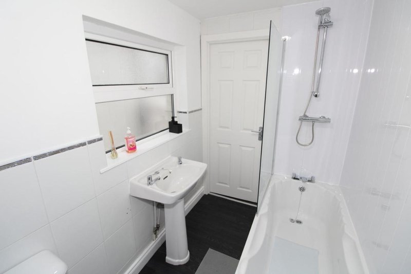White bathroom with pedestal sink, bathtub, shower enclosure and window