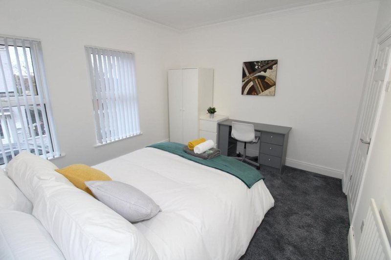 Bright bedroom with double bed, grey carpet, desk, and vertical blinds on windows