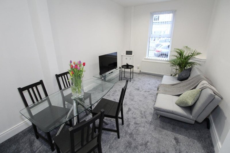 Modern open-plan living area with dining table, sofa, TV, and potted plants by window