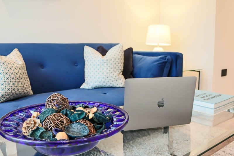 Modern living room with blue sofa, decorative cushions, laptop, and purple bowl on table