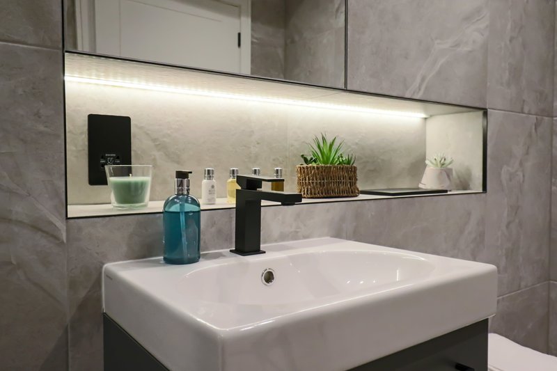 Modern bathroom with white basin, black tap, illuminated mirror shelf and grey tiled walls