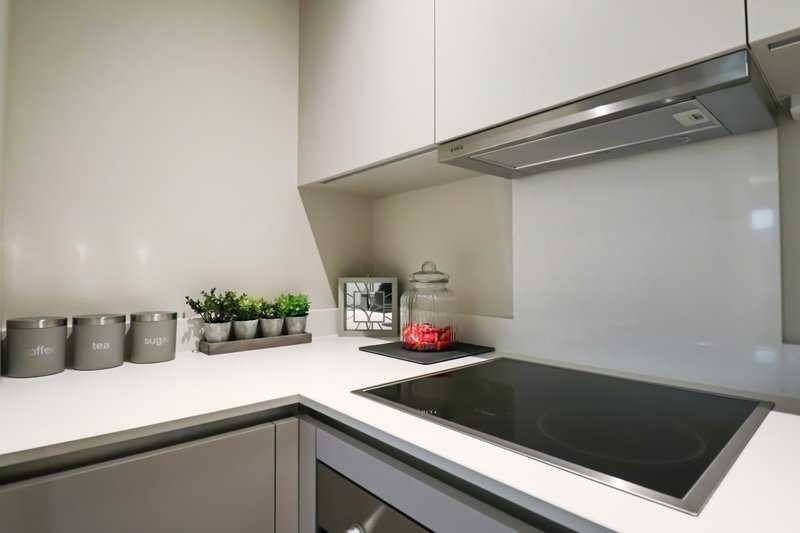 Modern kitchen with white countertop, induction hob, stainless steel extractor hood, and potted plants