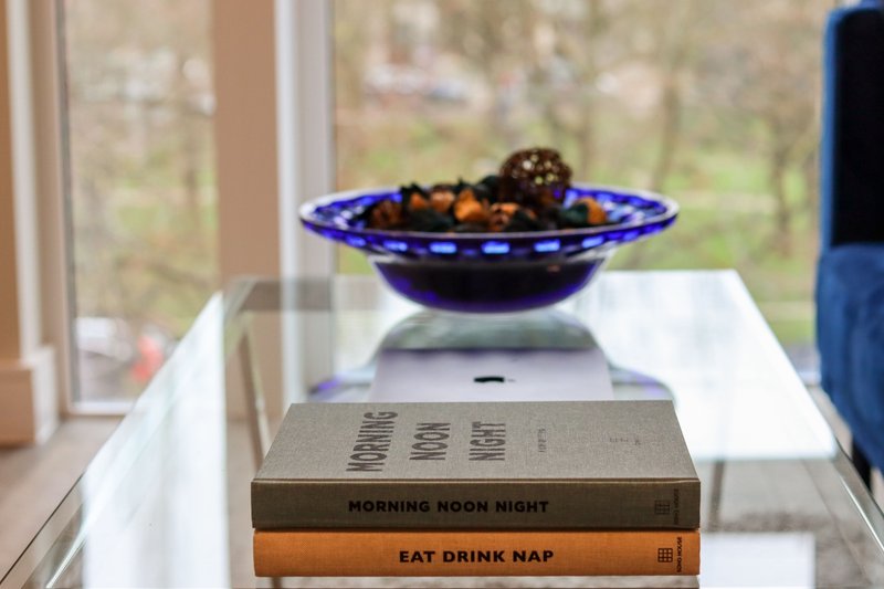 Windowsill with stacked books, blue decorative bowl with fruit, and garden view beyond