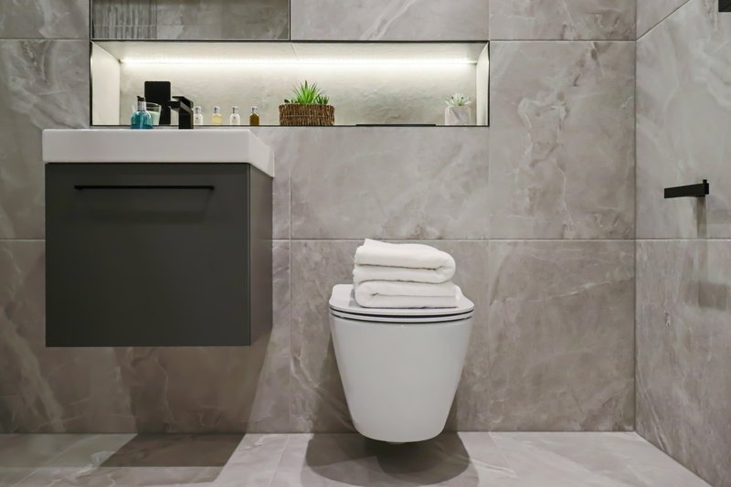 Modern bathroom with grey tile walls, wall-mounted black vanity, toilet, towels and mirror.