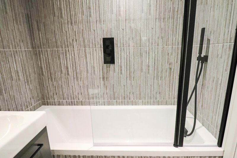 Modern bathroom with white bathtub, grey tile walls, and black shower fixtures