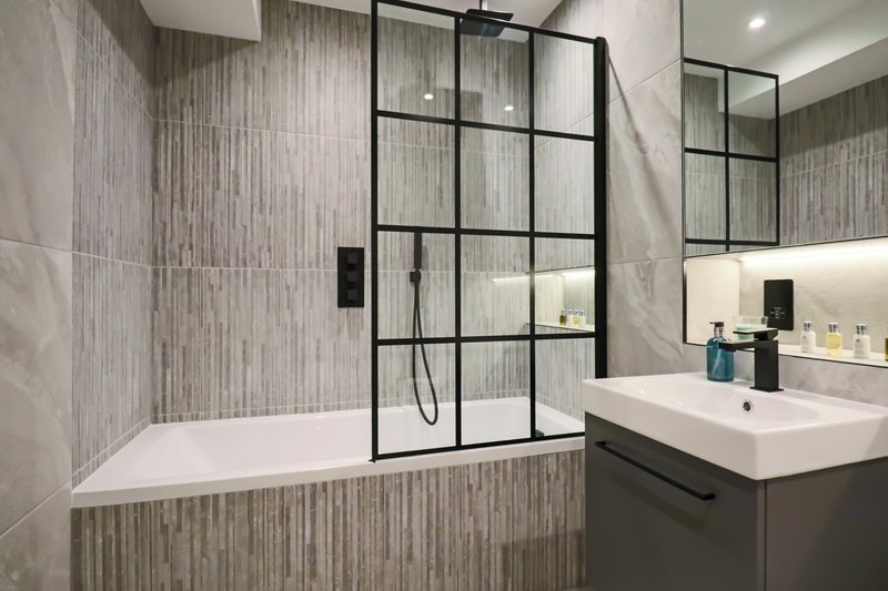 Modern bathroom with bathtub, black-framed glass shower enclosure, and dual vanity sinks