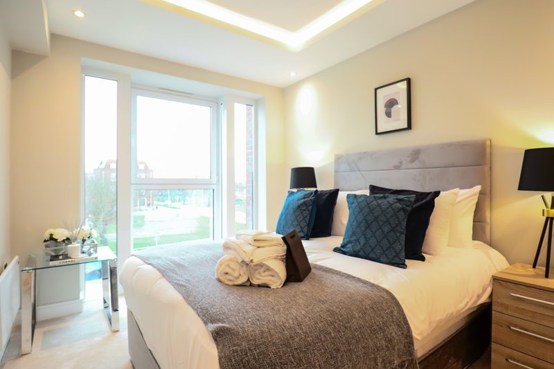Modern bedroom with double bed, cushions, wooden nightstands and balcony doors with views
