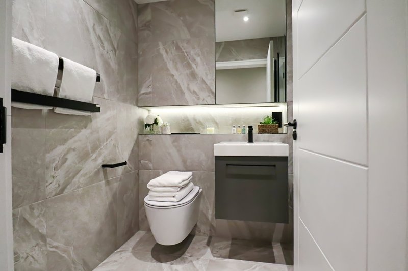 Modern bathroom with marble tile walls, white toilet, dark vanity sink and mirror
