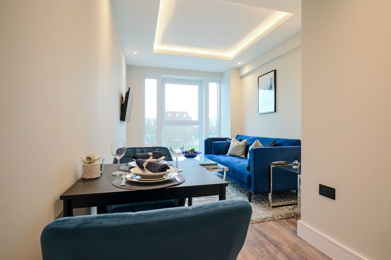 Modern living room with blue sofa, dining table, large windows and ceiling lighting