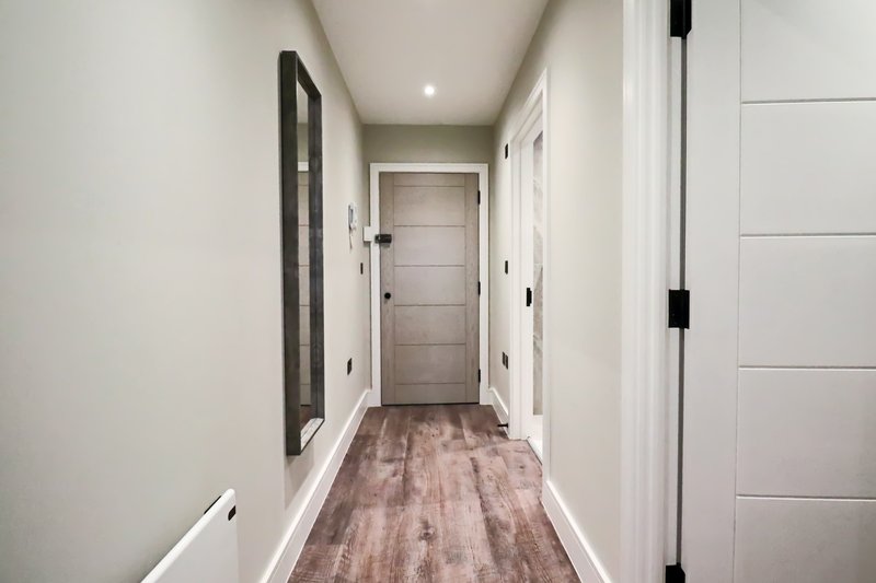 Long hallway with white walls, wooden floor, and multiple white doors