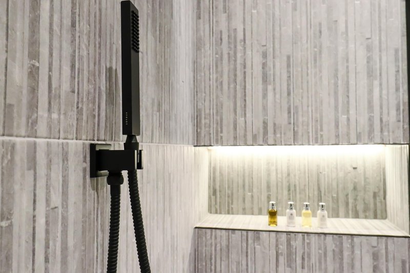 Modern bathroom with black rainfall showerhead, tiled walls, and recessed shelf with toiletries