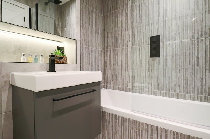 Modern bathroom with grey vanity unit, white sink, mirror, and bathtub with glass partition