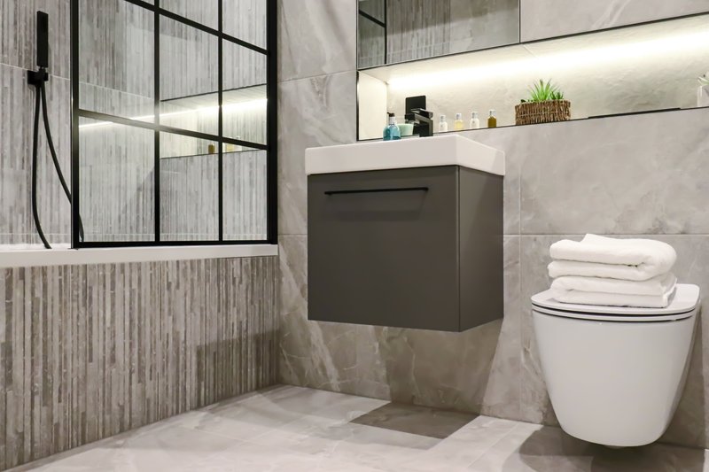 Modern bathroom with walk-in shower, vanity sink, toilet, and shelving with toiletries