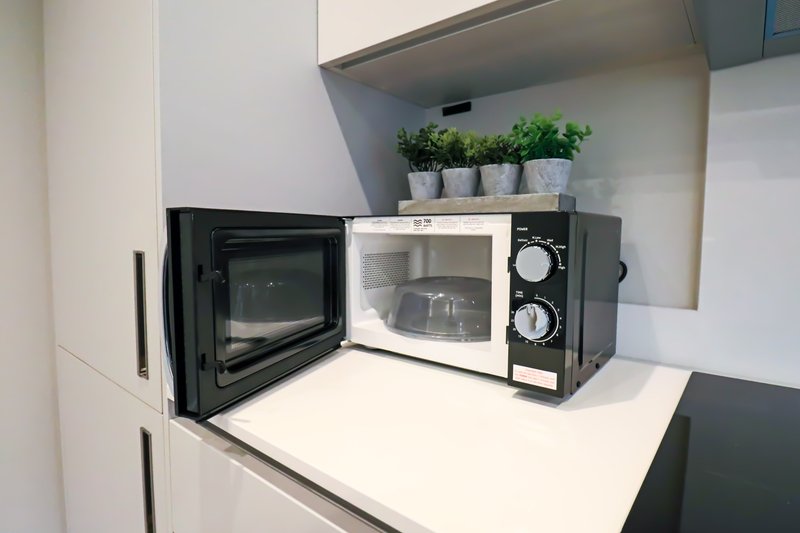 Kitchen counter with black microwave oven and potted plants on shelf above