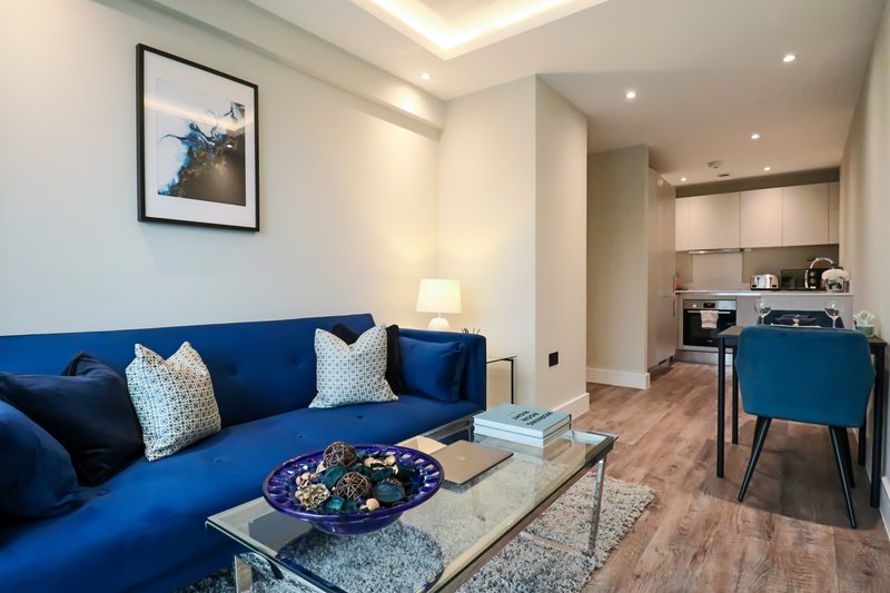 Modern living room with blue sofa, coffee table, framed artwork, and open-plan kitchen area
