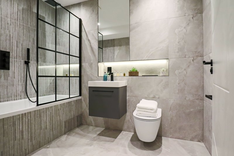 Modern bathroom with shower enclosure, dark vanity unit, toilet, and illuminated mirror