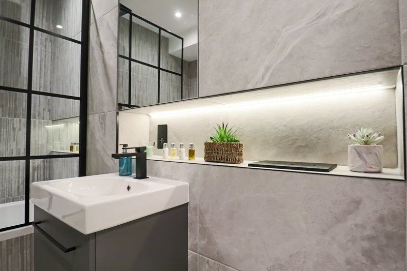 Modern bathroom with white basin, dark vanity, mirror and potted plants on shelf