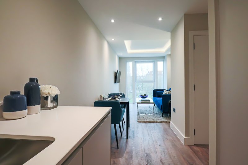 Modern open-plan kitchen and dining area with white counters, blue chairs, and large windows