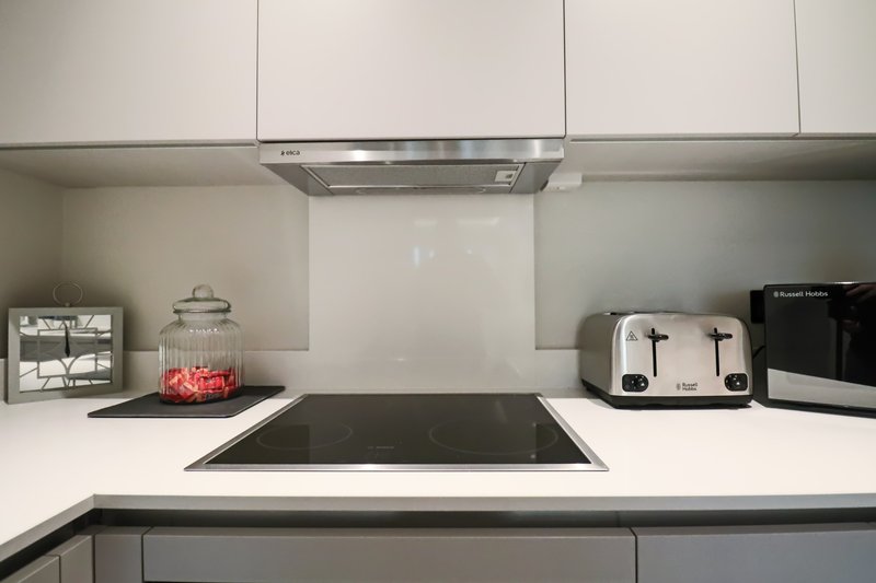 Modern kitchen with white cabinetry, stainless steel cooker hood, induction hob and white splashback