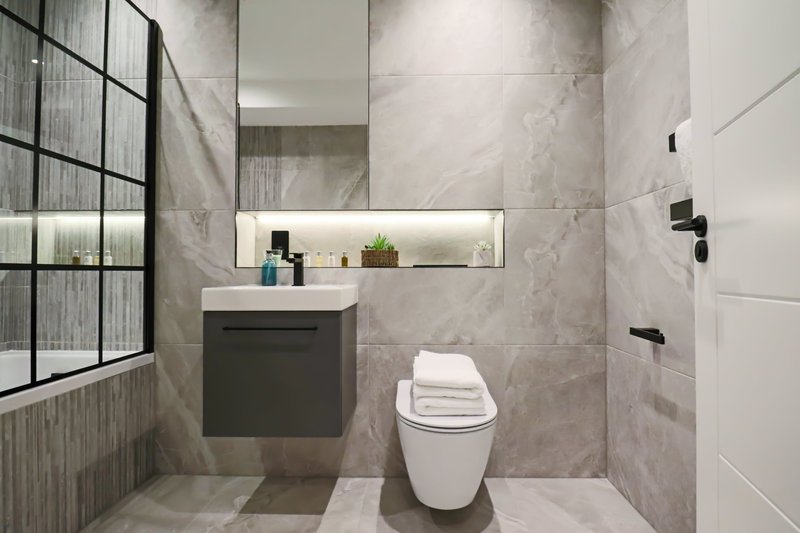 Modern bathroom with marble tile walls, white toilet, dark vanity sink and mirrored cabinet