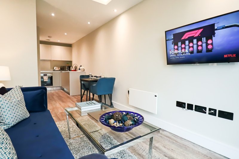 Open-plan living room with blue sofa, dining table, kitchen, wall-mounted TV and modern furnishings