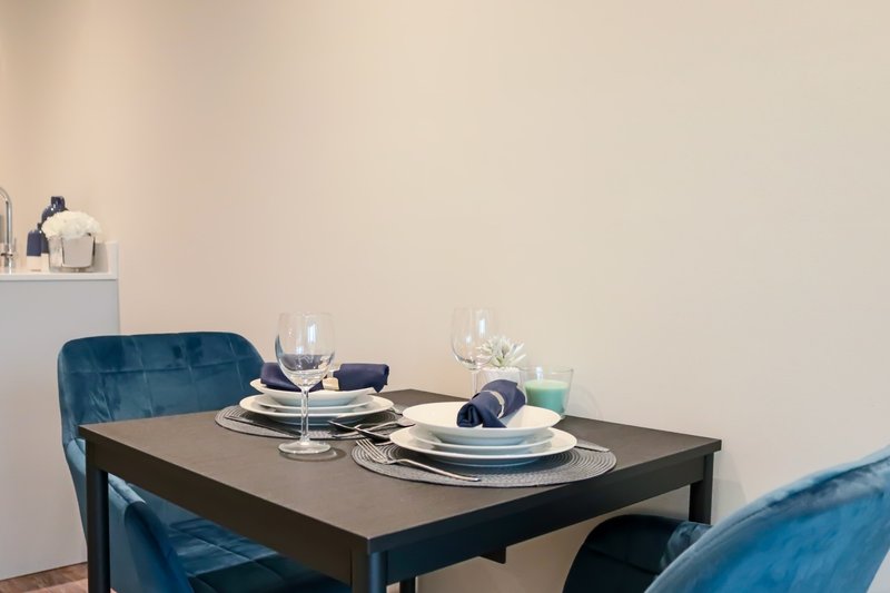 Dining table set for two with blue upholstered chairs and minimalist tableware